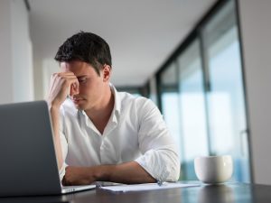 Frustrerad ung affärsman arbetar på laptop hemma